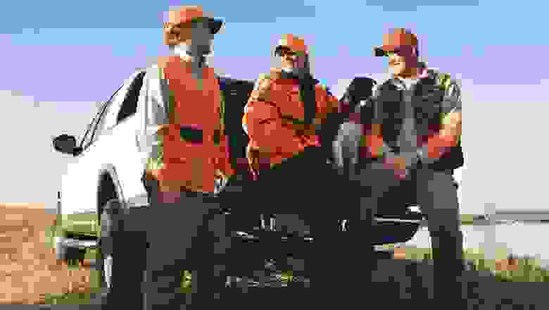 Three Hunters in Blaze Orange with their Bird Dog Sitting in the Back of a Pickup Truck Next to a Lake